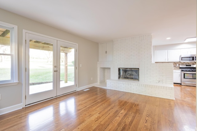 unfurnished living room featuring light wood-type flooring, visible vents, french doors, a fireplace, and baseboards