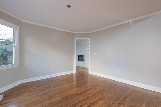 empty room featuring ornamental molding, a brick fireplace, baseboards, and wood finished floors