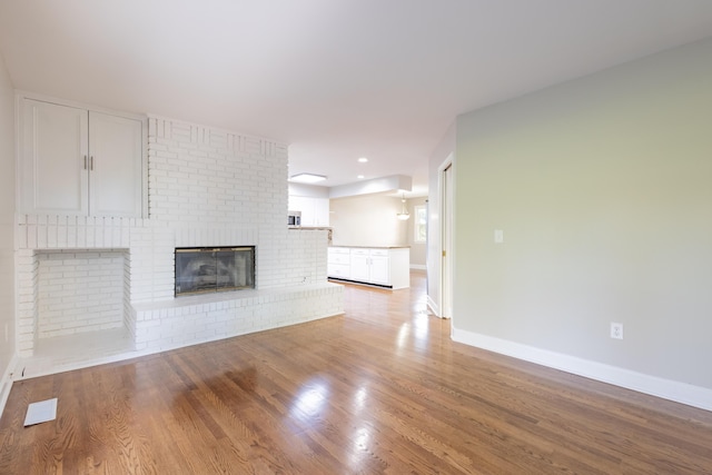 unfurnished living room featuring light wood finished floors, visible vents, a brick fireplace, and baseboards