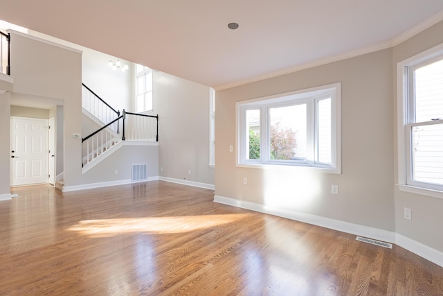 unfurnished living room with visible vents, ornamental molding, wood finished floors, baseboards, and stairs