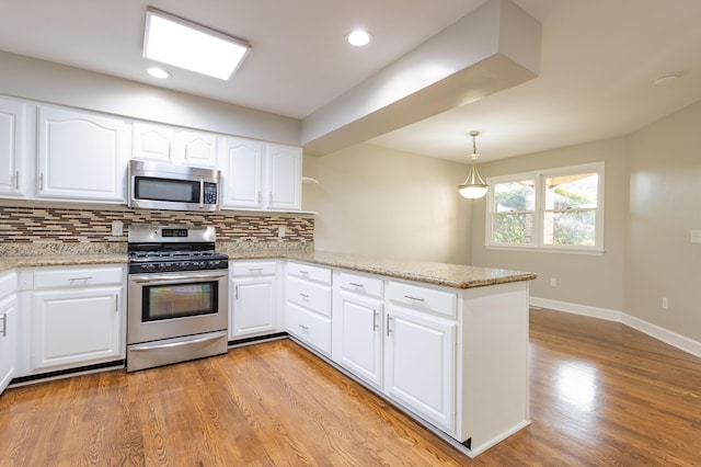 kitchen featuring light stone counters, a peninsula, stainless steel appliances, light wood-style floors, and tasteful backsplash