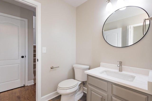 half bath with toilet, vanity, baseboards, and wood finished floors