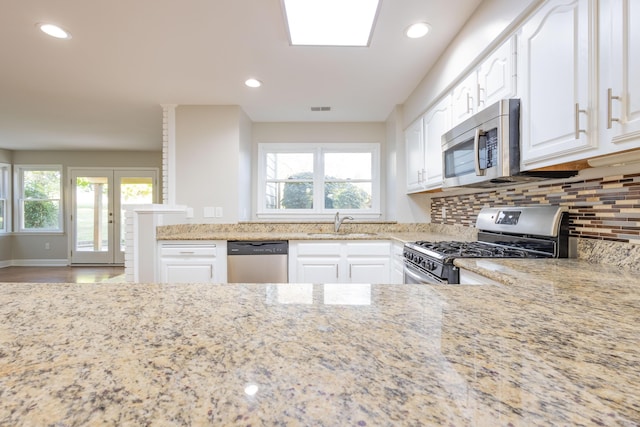 kitchen featuring a sink, tasteful backsplash, appliances with stainless steel finishes, white cabinets, and light stone countertops