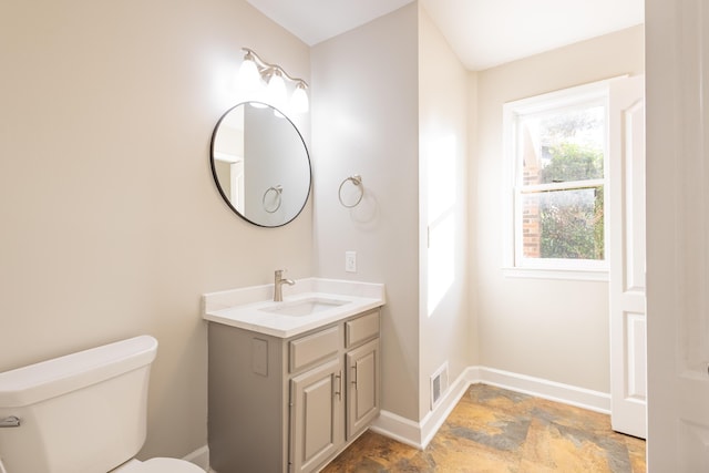 half bathroom featuring vanity, baseboards, visible vents, stone finish flooring, and toilet