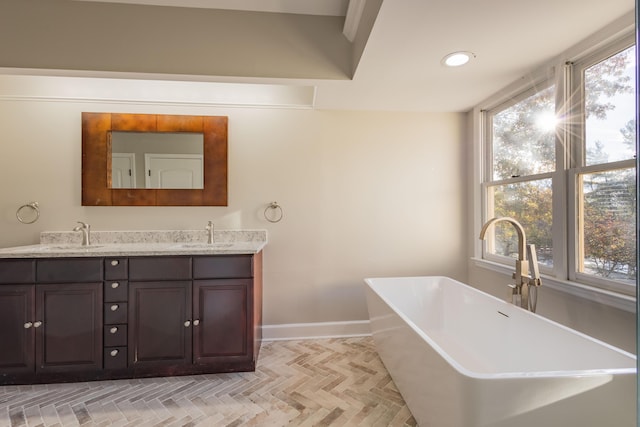 full bathroom with double vanity, a freestanding tub, a healthy amount of sunlight, and a sink