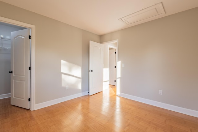 spare room featuring baseboards, light wood-style floors, and attic access