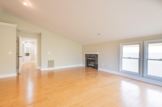 unfurnished living room with baseboards, light wood finished floors, visible vents, a high end fireplace, and vaulted ceiling