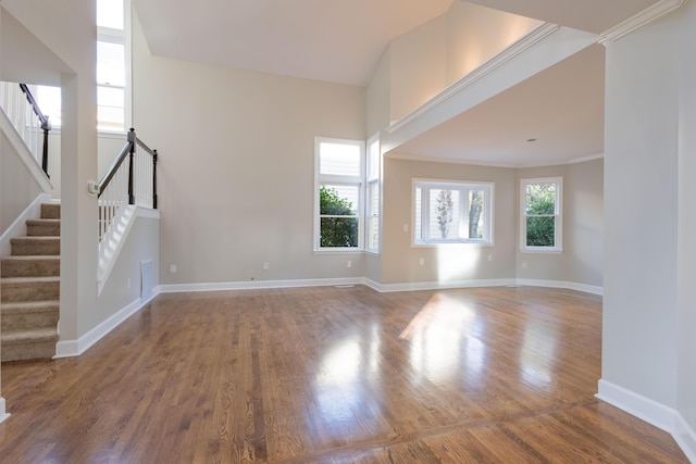 unfurnished living room with ornamental molding, wood finished floors, stairway, a high ceiling, and baseboards