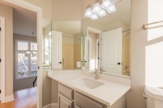 bathroom featuring a notable chandelier, toilet, wood finished floors, walk in shower, and vanity