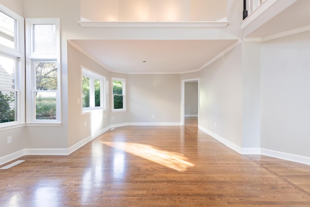 empty room with wood finished floors, baseboards, visible vents, a towering ceiling, and crown molding
