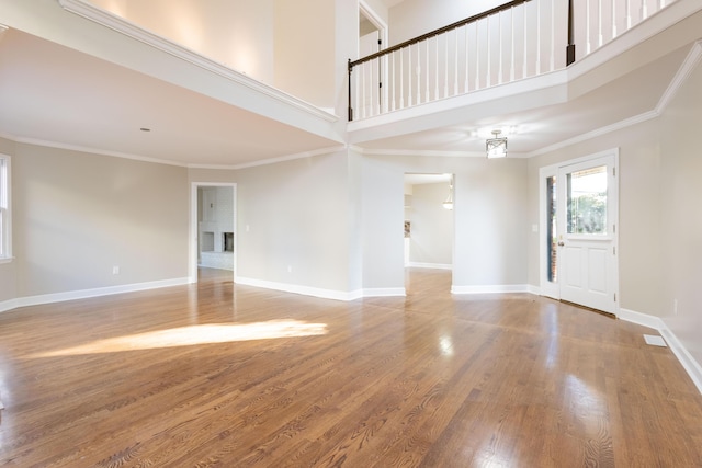 unfurnished living room featuring visible vents, baseboards, ornamental molding, a high ceiling, and wood finished floors