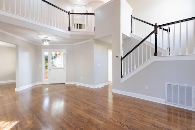 entrance foyer featuring visible vents, crown molding, baseboards, a towering ceiling, and wood finished floors