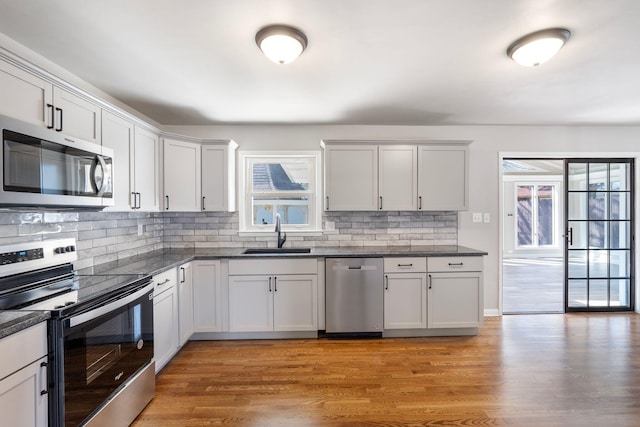 kitchen with light wood-style flooring, a sink, backsplash, stainless steel appliances, and dark stone counters