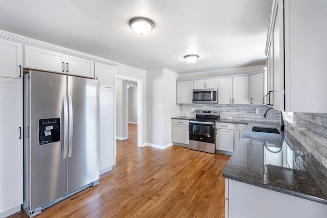 kitchen featuring backsplash, light wood-type flooring, stainless steel appliances, white cabinetry, and a sink