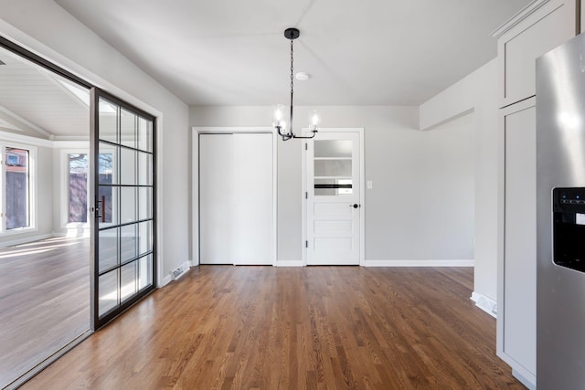 unfurnished dining area with wood finished floors, baseboards, and a chandelier