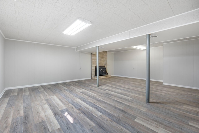 finished basement featuring visible vents, a wood stove, wood finished floors, and baseboards