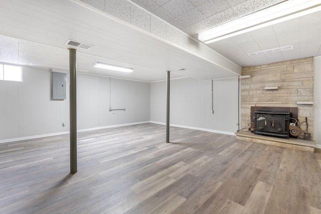 basement with electric panel, visible vents, baseboards, and wood finished floors