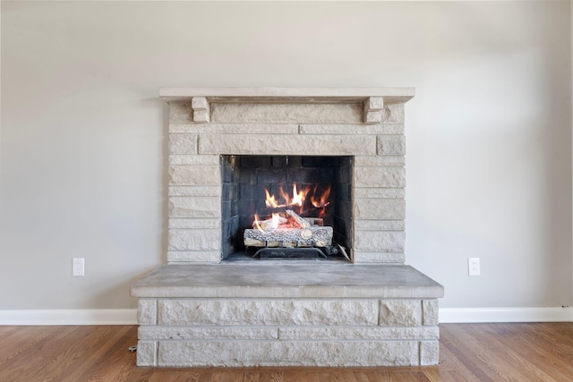 details with baseboards, a stone fireplace, and wood finished floors