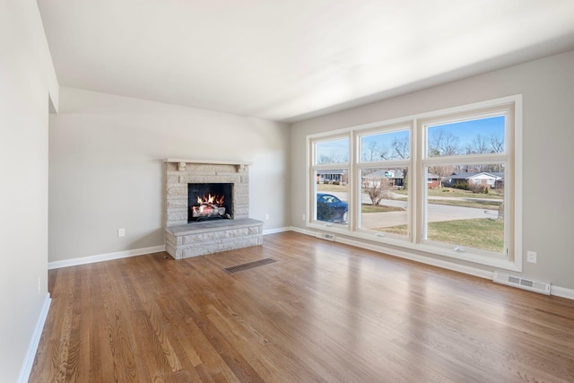 unfurnished living room featuring a stone fireplace, wood finished floors, and visible vents