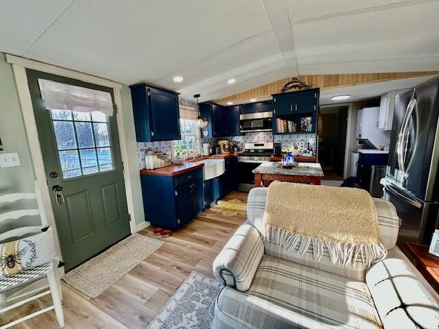 kitchen featuring blue cabinetry, appliances with stainless steel finishes, light wood-style floors, and vaulted ceiling