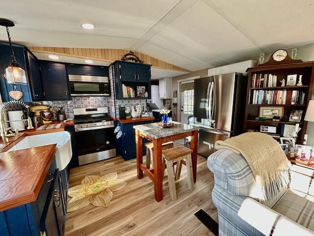 kitchen featuring wood counters, lofted ceiling with beams, appliances with stainless steel finishes, light wood-style floors, and blue cabinets