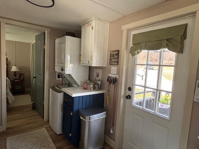 kitchen featuring blue cabinets, wood finished floors, stacked washing maching and dryer, white cabinetry, and light countertops