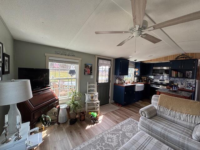 living area with ceiling fan, lofted ceiling, light wood finished floors, and a textured ceiling