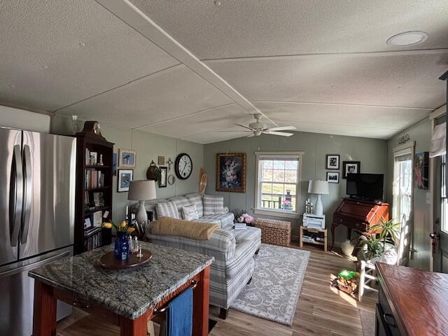 living room featuring ceiling fan, lofted ceiling, a textured ceiling, and wood finished floors