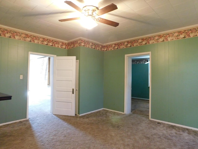 carpeted empty room with baseboards, ceiling fan, and crown molding