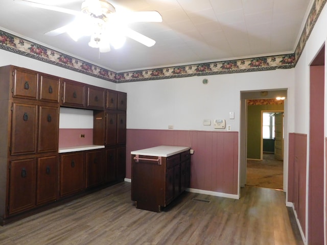 kitchen with dark brown cabinets, light countertops, ornamental molding, and wood finished floors