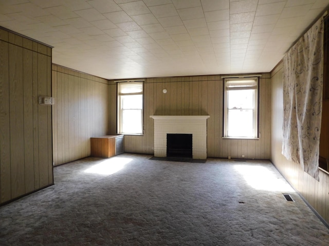 unfurnished living room featuring a brick fireplace, visible vents, a wealth of natural light, and carpet floors