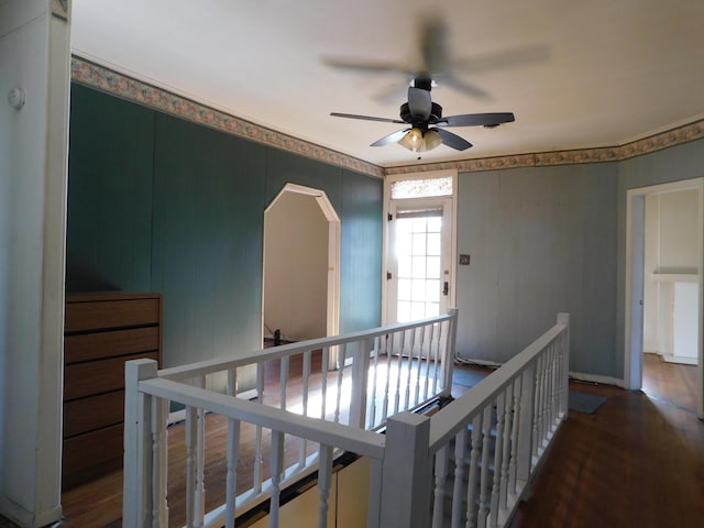 corridor with wood finished floors, an upstairs landing, and arched walkways