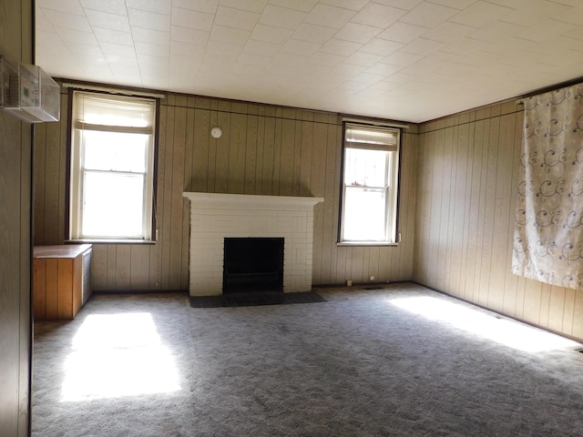 unfurnished living room with a healthy amount of sunlight, a fireplace, wood walls, and carpet