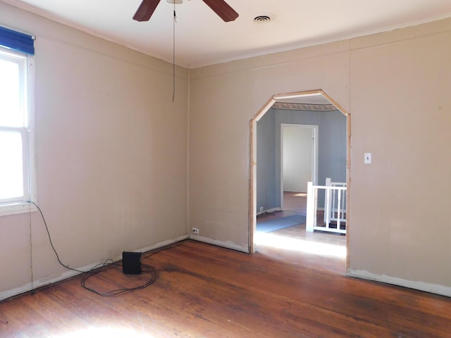 unfurnished room with arched walkways, wood finished floors, visible vents, and ceiling fan