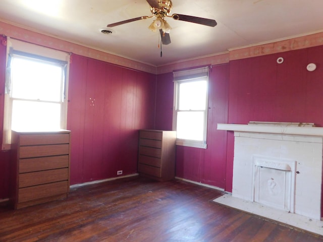 unfurnished living room featuring a ceiling fan, wood finished floors, visible vents, a fireplace, and ornamental molding