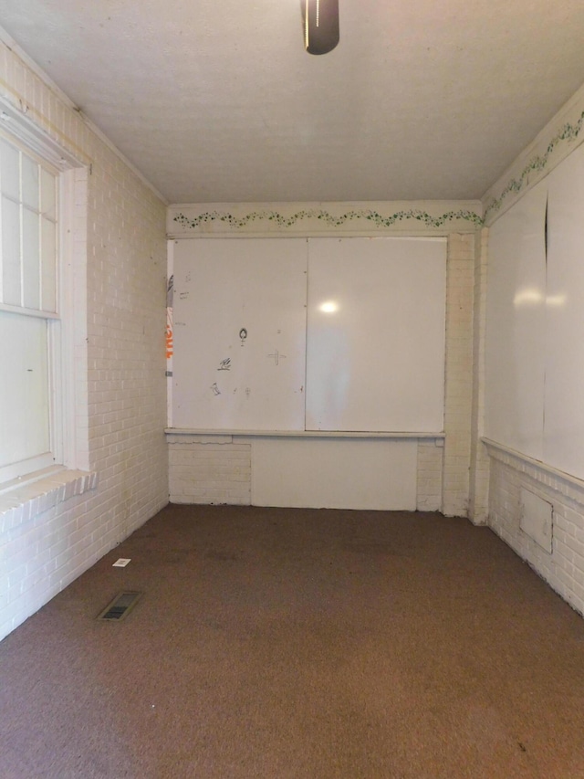 carpeted spare room featuring visible vents and brick wall