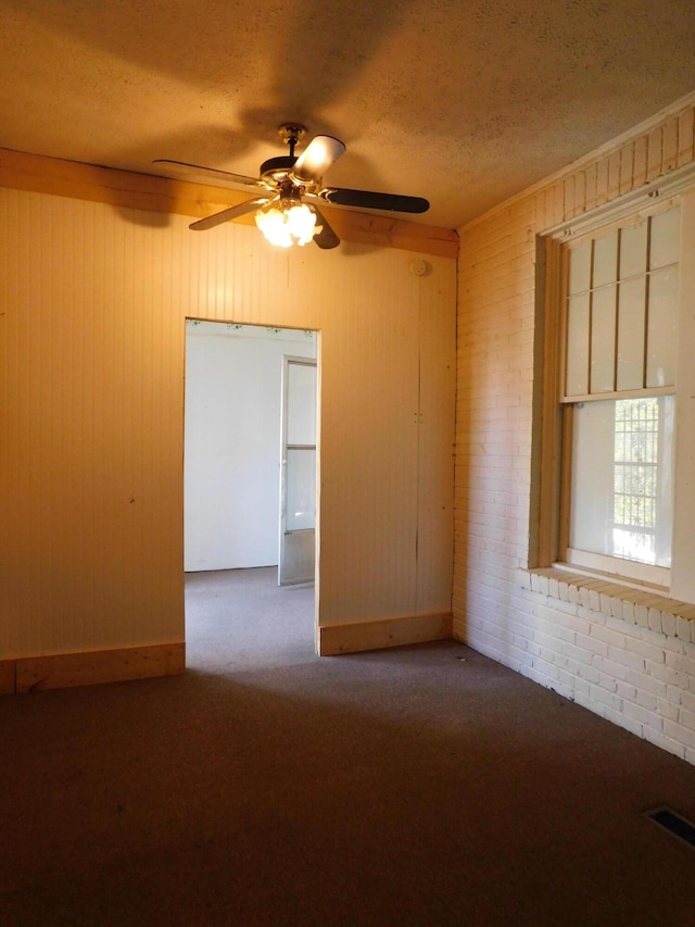 carpeted spare room with ceiling fan, visible vents, brick wall, and a textured ceiling