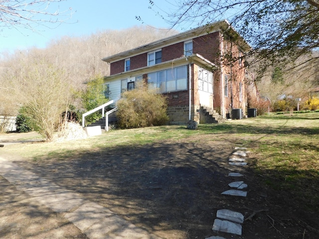 view of side of home featuring brick siding, a lawn, and cooling unit