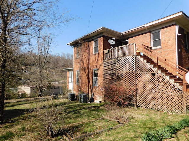 view of side of property with stairway, cooling unit, brick siding, and a yard