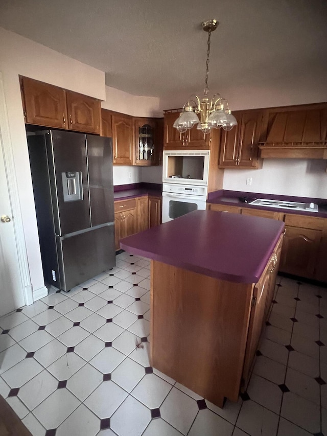 kitchen with dark countertops, a kitchen island, white appliances, wall chimney exhaust hood, and light floors