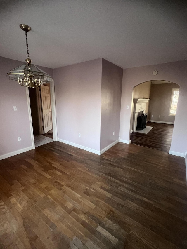 empty room featuring baseboards, dark wood-type flooring, and an inviting chandelier