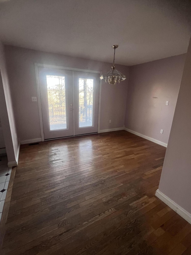 unfurnished dining area featuring an inviting chandelier, wood finished floors, and baseboards