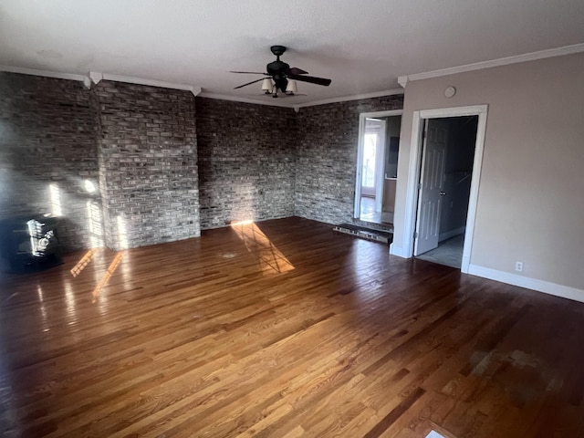 spare room with ornamental molding, wood finished floors, brick wall, baseboards, and ceiling fan