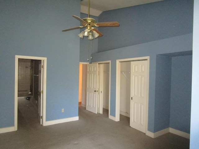 unfurnished bedroom featuring a ceiling fan, baseboards, carpet floors, high vaulted ceiling, and multiple closets