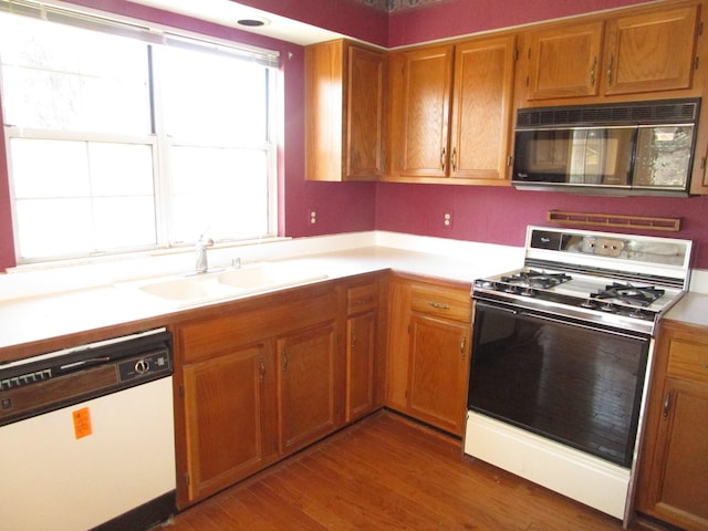 kitchen with white appliances, dark wood-style floors, brown cabinetry, a sink, and light countertops