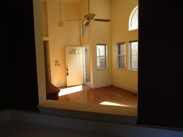 foyer featuring ceiling fan, baseboards, wood finished floors, and a towering ceiling