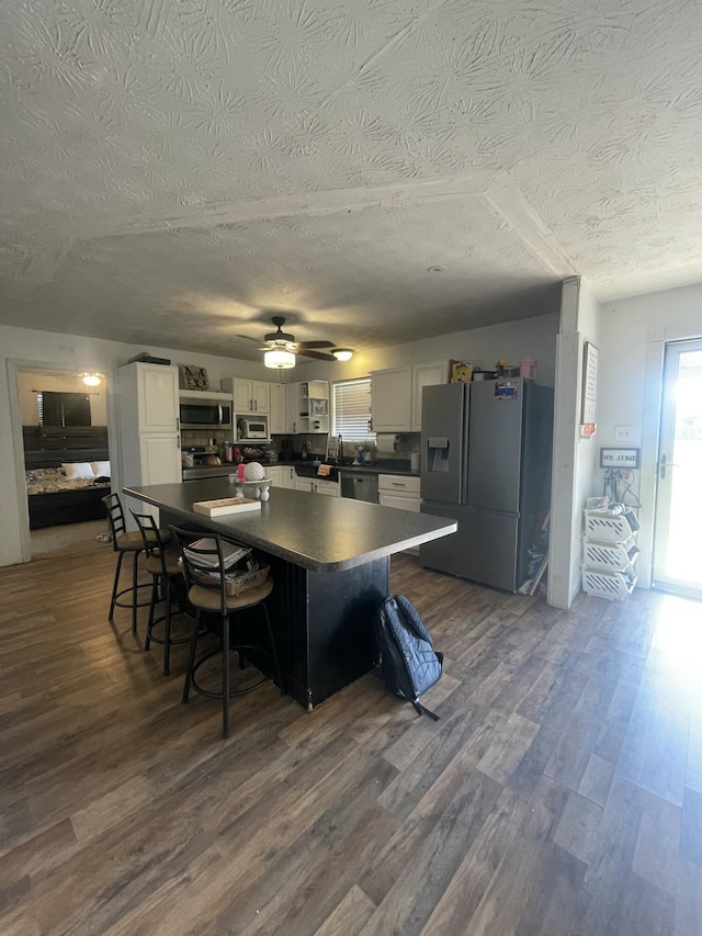 kitchen with dark wood-type flooring, dark countertops, a kitchen island, white cabinetry, and appliances with stainless steel finishes