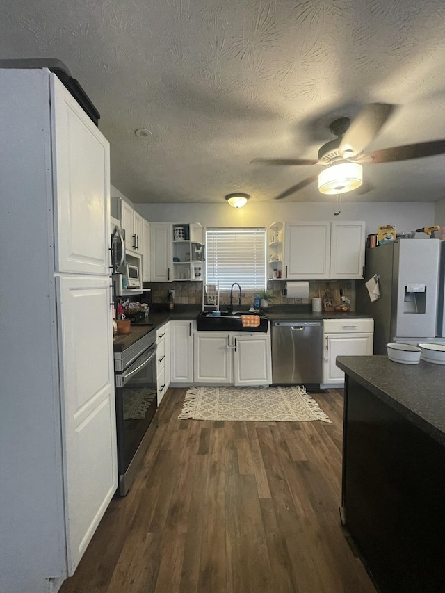 kitchen featuring dark countertops, a sink, appliances with stainless steel finishes, and open shelves