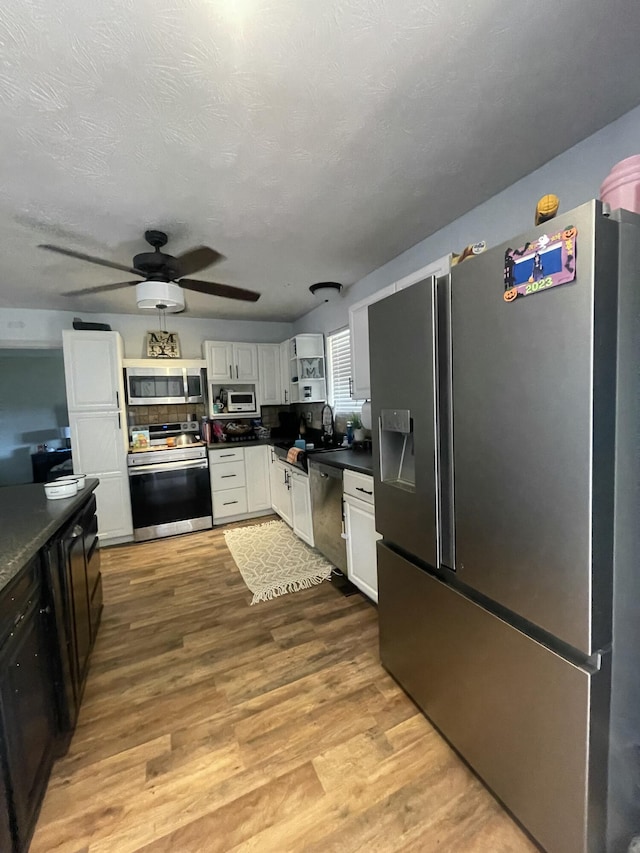 kitchen featuring dark countertops, white cabinets, appliances with stainless steel finishes, and wood finished floors