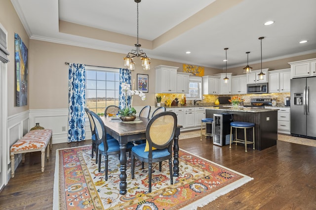 dining room featuring a tray ceiling, crown molding, dark wood-type flooring, and wainscoting